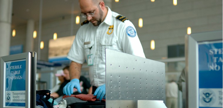 A TSA agent searches luggage at an airport.  Carolina K. Smith MD / Shutterstock.com